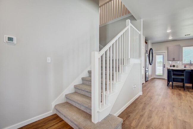 Carpeted staircase with white balusters leading to open concept living area and modern kitchen beyond