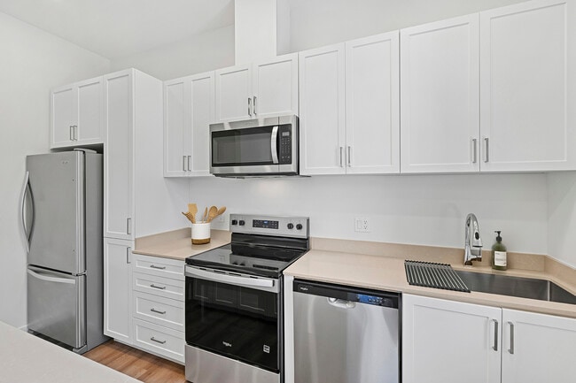 Cocina independiente con electrodomésticos de acero inoxidable, gabinetes blancos, encimeras de cuarzo beige y pisos de superficie dura. - eaves San Marcos