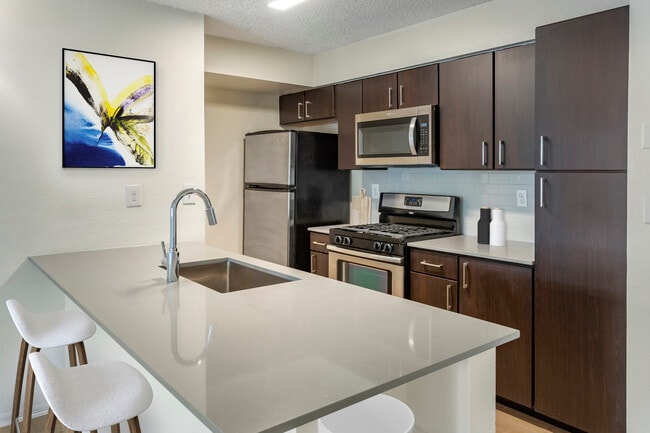 Renovated Package II kitchen with espresso cabinetry, grey quartz countertops, stainless steel appliances, tile backsplash, and hard surface plank flooring
