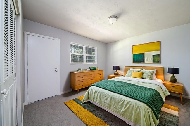 Bright modern bedroom featuring a cozy double bed with green and yellow accents, elegant wooden furniture, and vibrant wall art.