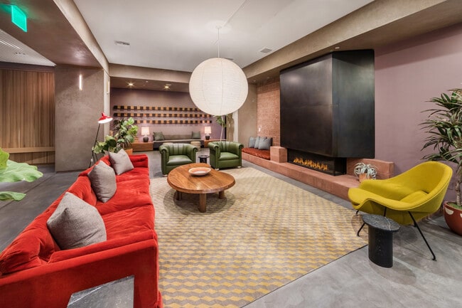 Espacio de estar acogedor con asientos en tonos rojos y verdes vibrantes, una chimenea moderna y una elegante mesa de café redonda bajo una elegante lámpara colgante.