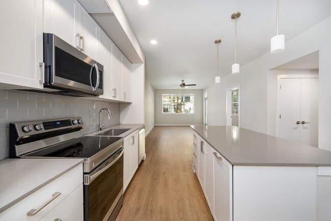 Finish Package I Kitchen with white cabinetry, grey quartz countertops, grey tile backsplash, stainless steel appliances, and hard-surface vinyl plank flooring