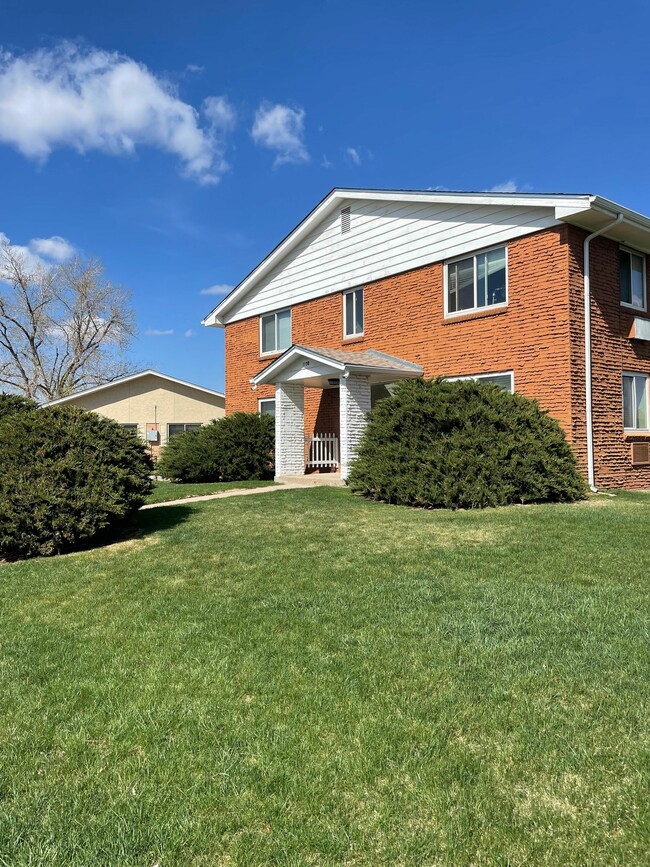 Inviting brick apartment building with manicured lawn and bright windows under a clear blue sky. - Allison West Apartments