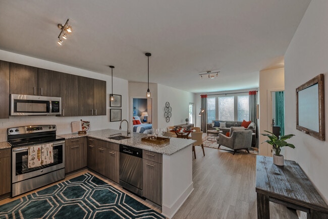 Open concept kitchen with brown cabinetry, granite countertops, stainless steel appliances, tile backsplash and hard surface flooring
