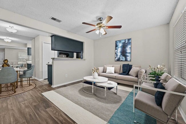 Living room with beige sofa, white coffee table, ceiling fan, framed wall art, and open view to dining area and kitchen