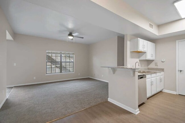 Open living and kitchen area with breakfast bar, white cabinetry, ceiling fan, and large window bringing in natural light