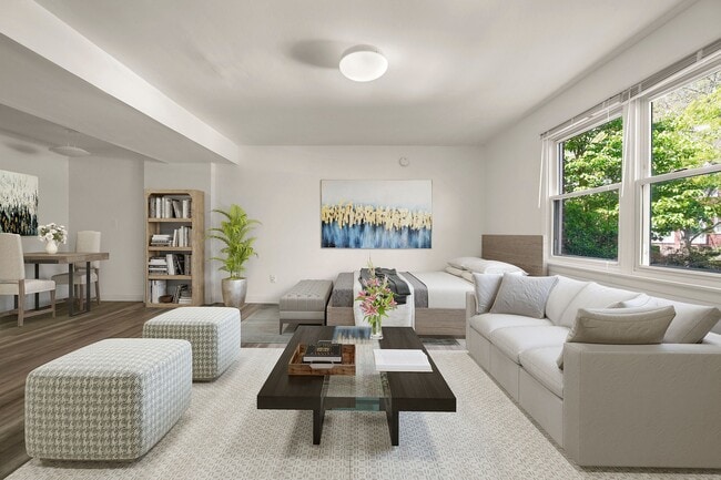 Inviting studio apartment with plush gray sofas, chic decor, and large windows offering lush garden views, perfect for relaxation and entertainment.