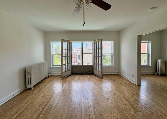 Bright and airy living space with wooden floors, large windows, and elegant French doors offering a charming view of the neighborhood.