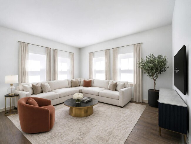 Light-filled living room with expansive corner windows, warm flooring, and ample seating designed for gathering, relaxing, and everyday comfort. - Modera Weston