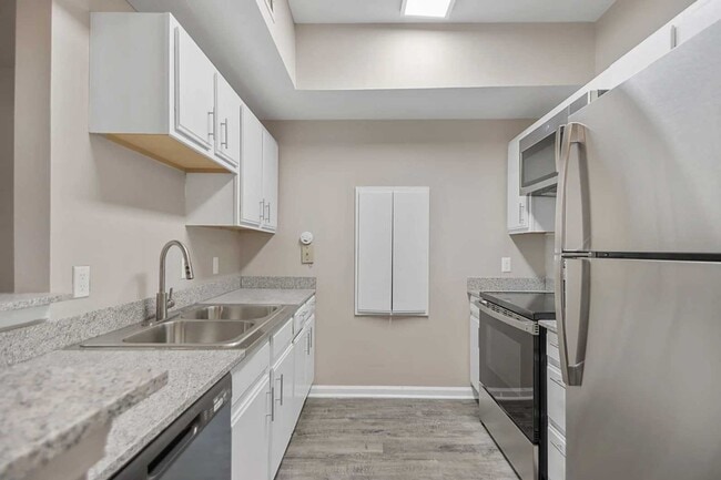 Galley style kitchen with double sink, stainless steel appliances, white cabinetry, and wood style flooring in bright layout