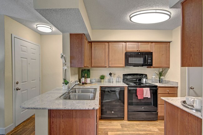 Una cocina con armarios de luces y electrodomésticos negros - Motif Apartamentos