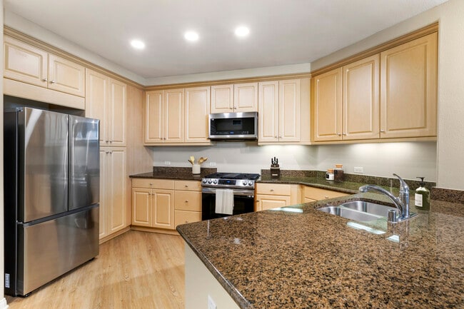 Renovated Package I kitchen with stainless steel appliances, brown speckled granite, oak cabinetry, and hard surface flooring