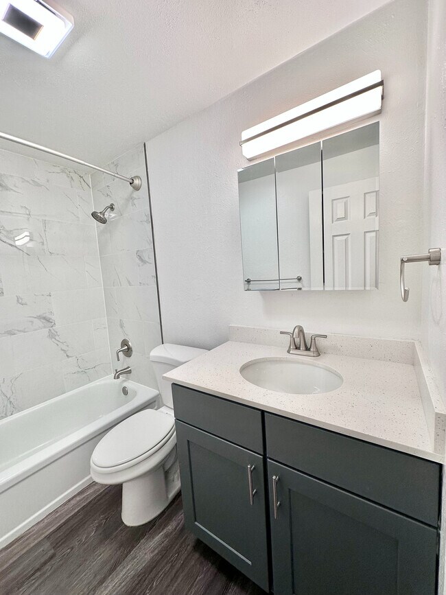Elegant bathroom with modern fixtures, featuring marble-tiled shower, stylish vanity with mirror, and sleek wood flooring.
