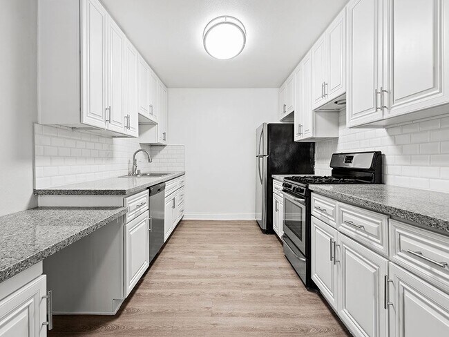 Large white tiled kitchen with stainless steel oven, microwave, and fridge.