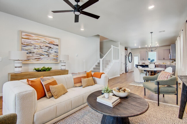 Open concept living room with white sofa, accent pillows, ceiling fan, and view into dining area and kitchen