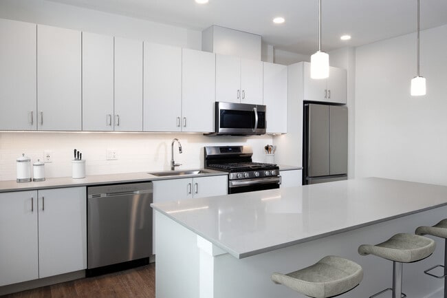 Design Collection I (North Building) Kitchen with light grey cabinetry, white tile backsplash, grey quartz countertops, stainless steel appliances, and hard surface flooring