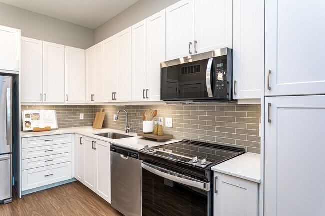 Modern kitchen with white cabinetry, undercabinet lighting, grey tile backsplash, and white quartz countertops