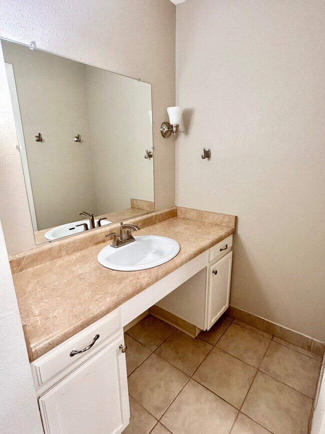 Baño moderno con elegante encimera beige, elegante lavabo bajo encimera y gran espejo de pared para una sensación de amplitud.