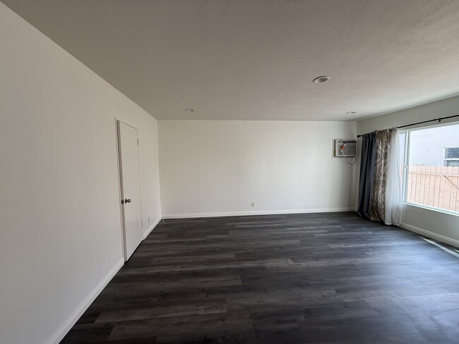 Large living room with new floors and paint and ample natural light with large windows. - 5462 Barton Ave Apartment Unit 1