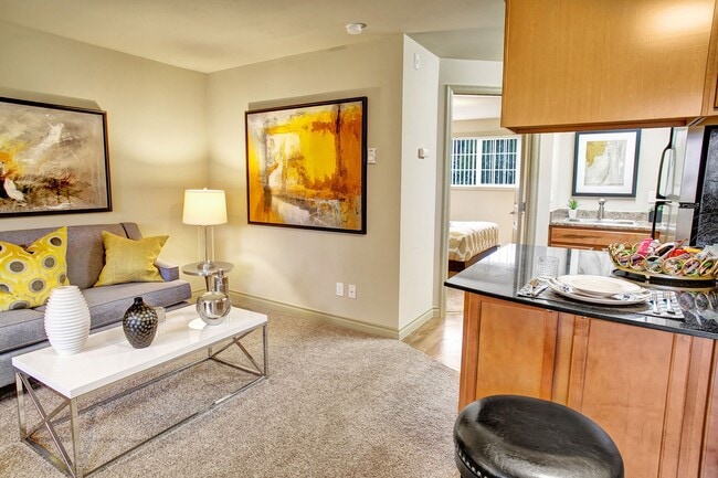 A living room with couch, coffee table, and view into the kitchen - Colonial Square