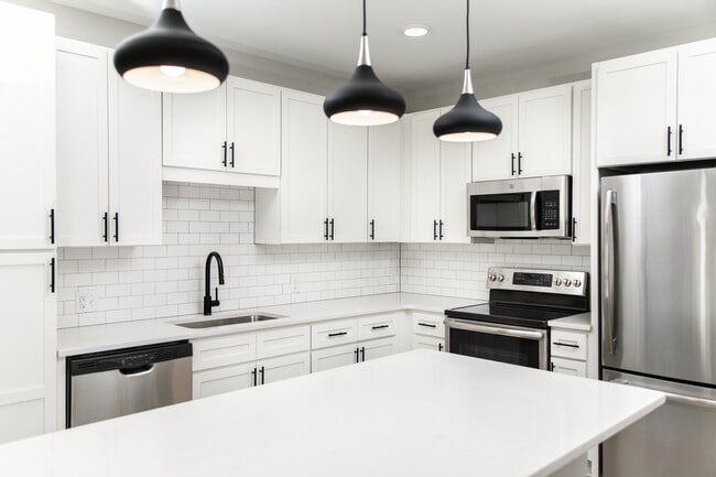 Kitchen with white quartz countertops, white cabinetry, and stainless steel appliances - Avalon South End Apartments