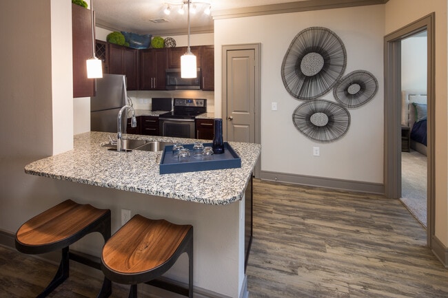 Modern kitchen with wood cabinetry, white tile backsplash, granite countertops, stainless steel appliances, and hard-surface flooring
