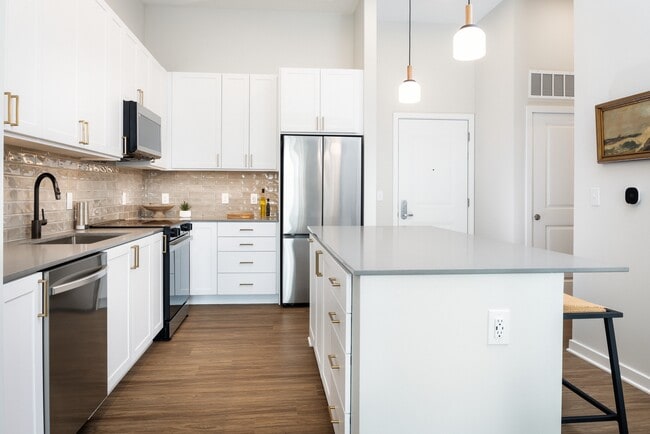 Design Collection I kitchen with white cabinetry, beige tile backsplash, grey quartz countertops, pendant lighting and hard surface flooring