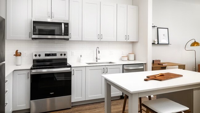 Design Collection II kitchen with stainless steel appliances, grey cabinetry, white tile backsplash, white quartz countertops, and hard surface flooring (representative photo) - Avalon Quincy Adams
