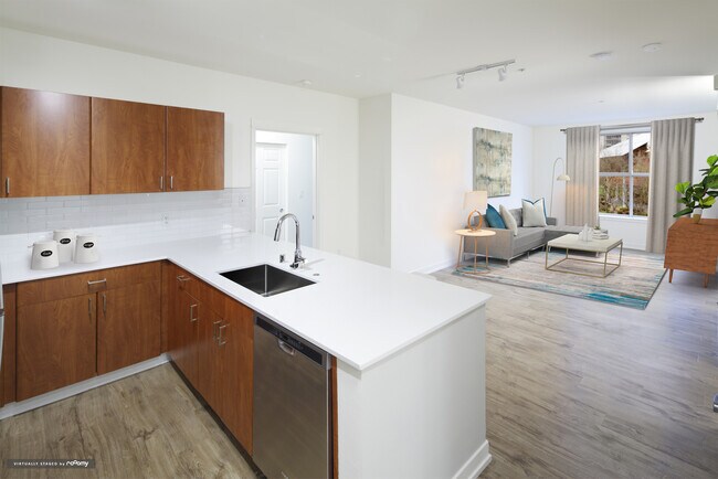 Renovated Package I kitchen and living area with white quartz countertops, oak cabinetry, stainless steel appliances, tile backsplash, and hard surface flooring