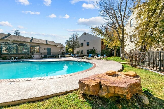Community swimming pool with concrete surround, blue lounge chairs, mature trees, and adjacent clubhouse
