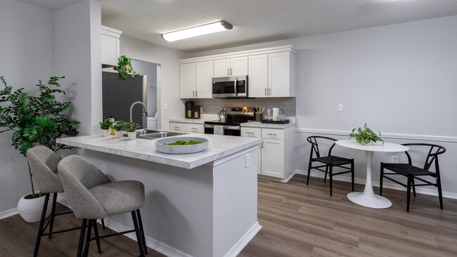 Enjoy the contemporary design of this kitchen featuring a breakfast bar, stainless steel appliances, and a comfortable dining area. - The Avenue Apartments