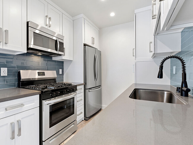 Blue tiled kitchen with quartz stone counters and stainless steel microwave, oven, fridge, and fixtures. - Cedar Glen Apartments