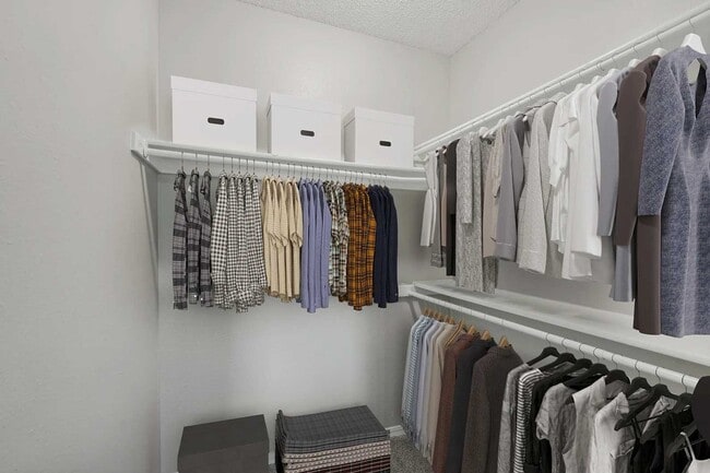 Spacious walk-in closet with double hanging rods, upper storage shelf with white boxes, and carpet flooring