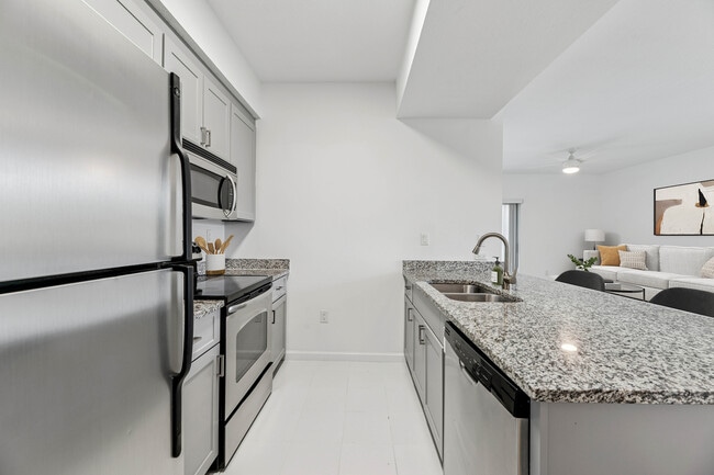 Renovated Package I kitchen with stainless steel appliances, tile backsplash, granite countertops (in most homes), and grey cabinetry