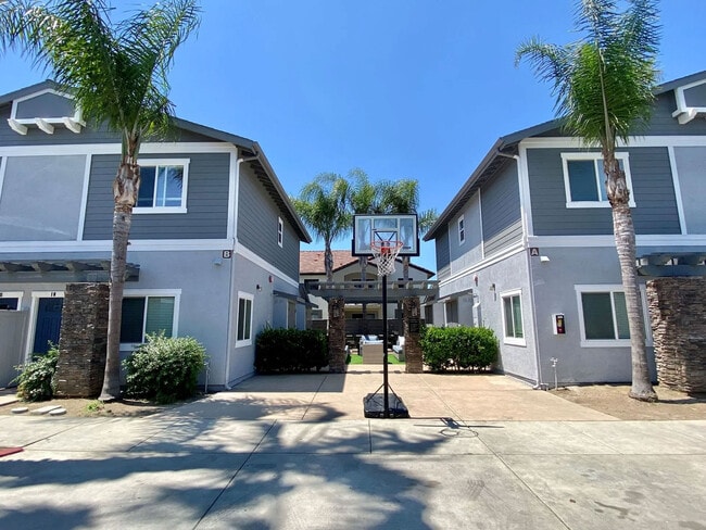 Área comunitaria con aro de baloncesto y zona de estar al fondo en The Nines Townhomes en Escondido, California. - The Nines Townhomes