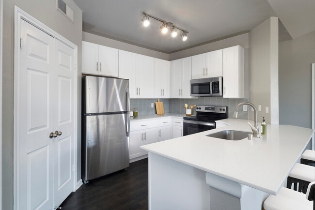 Classic Package II kitchen with stainless steel appliance, white quartz countertop, tile backsplash, white cabinetry, and hard-surface flooring - Avalon Addison