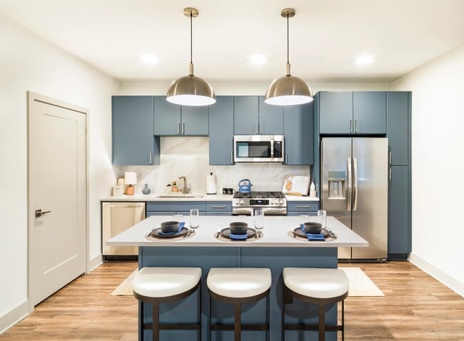 Cocina de diseño profesional con acabados de primera calidad, que incluyen armarios pintados, superficies que imitan la piedra, electrodomésticos de acero inoxidable e iluminación colgante de diseño. - Modera Westside Trail