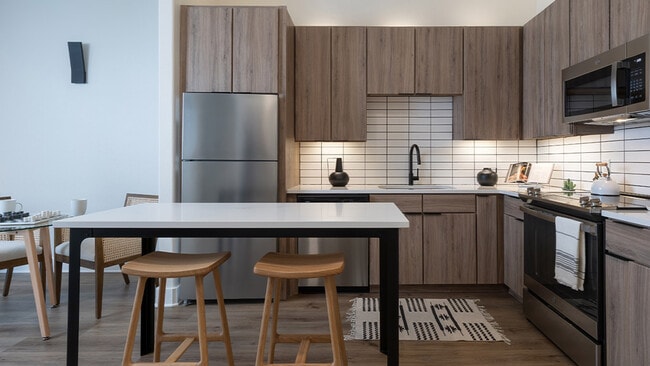 Cocina del apartamento con electrodomésticos de acero inoxidable, encimeras de cuarzo y suelos de madera.
