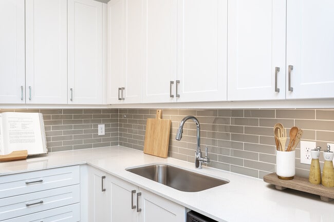 Kitchen with white cabinetry, grey tile backsplash, white quartz countertops, and undercabinet lighting