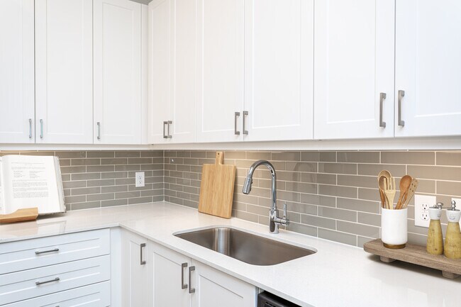 Kitchen with white cabinetry, grey tile backsplash, white quartz countertops, and undercabinet lighting - Avalon Carmel Commons