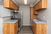 Galley kitchen with wood cabinetry, gray countertops, double sink, electric range, and full size refrigerator