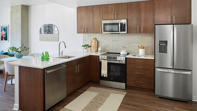 Apartment kitchen with stainless steel appliances, quartz countertops, and wood-style flooring. - Griffis Platform Union Station Apartments