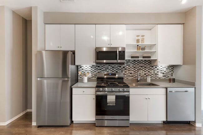 Renovated Package I kitchen with stainless steel appliances, dark quartz countertops, white cabinetry, tile backsplash, and hard surface flooring - AVA Somerville Apartments