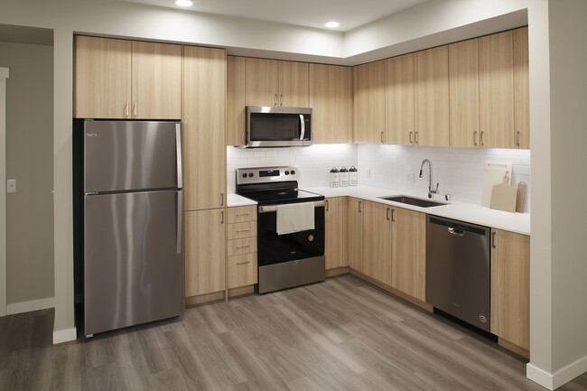 Phase II - Scheme D Kitchen with oak cabinetry, white tile backsplash, stainless steel appliances, white quartz countertops, and hard surface flooring - Avalon Newcastle Commons Apartments