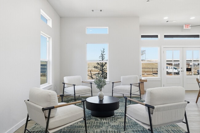 Bright and inviting lounge area with modern white armchairs, natural light flooding in through large windows, and a stylish round black coffee table.