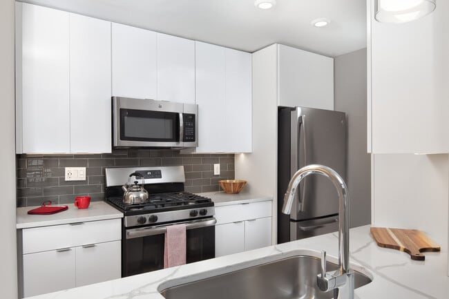 Premier Scheme kitchen with flat white cabinetry, white marbled quartz countertops, grey subway tile backsplash, stainless steel appliances, and hard surface flooring