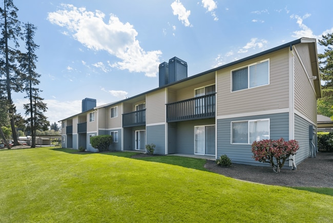 Appealing apartment building with carport parking, landscaped greenery, and a clear blue sky backdrop.