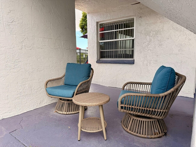 Charming patio corner featuring two stylish wicker chairs with teal cushions and a matching round table, perfect for relaxing.