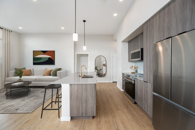 Signature Collection kitchen with dark cabinetry, marbled quartz countertops and backsplash, upgraded stainless steel appliances, and pendant lighting.