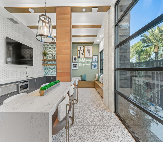 Chic modern kitchen with a stylish island, elegant lighting, and cozy seating area with a scenic view through large window. - Elan Crown Point